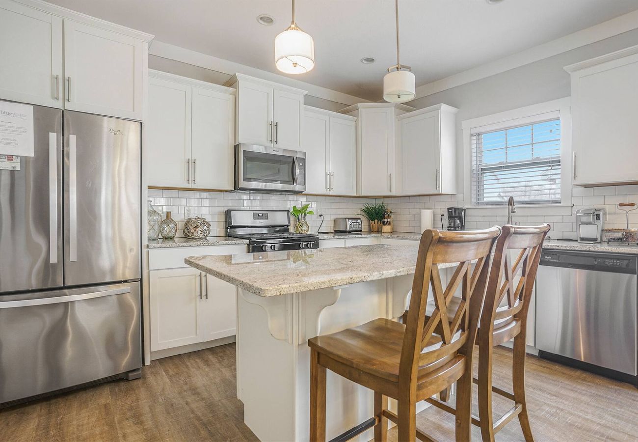 White kitchen with stainless steel appliances, granite island, and wooden barstools at Bridgewater Cottage