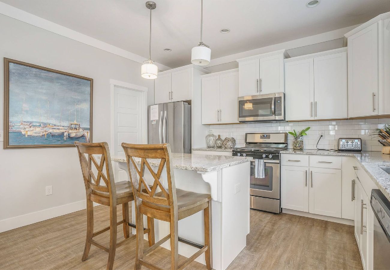 Kitchen with white cabinets, stainless steel appliances, granite island, and two barstools at Bridgewater Cottage