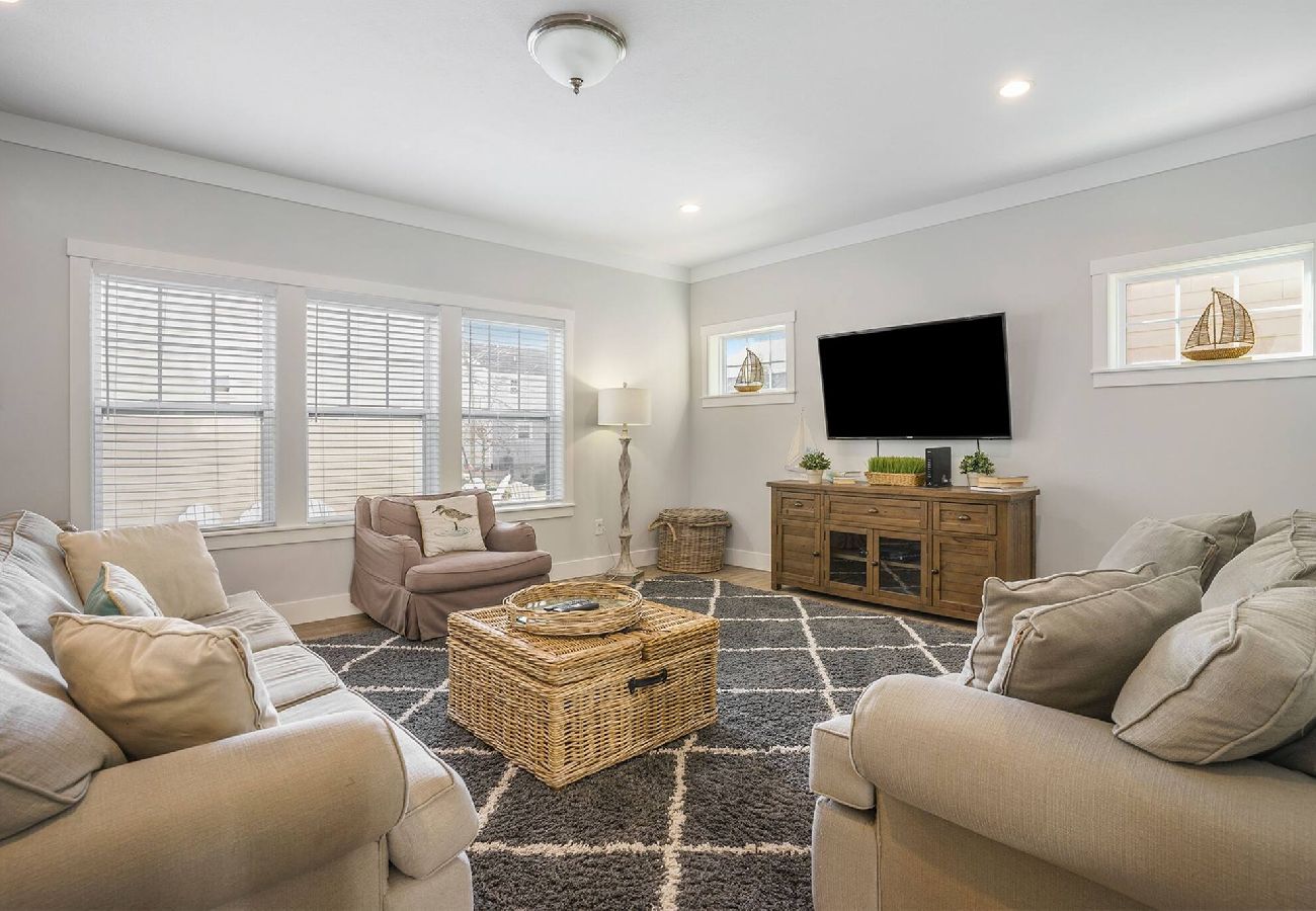 Living room with sofas, accent chair, large Tv, wicker coffee table, and bright windows at Bridgewater Cottage