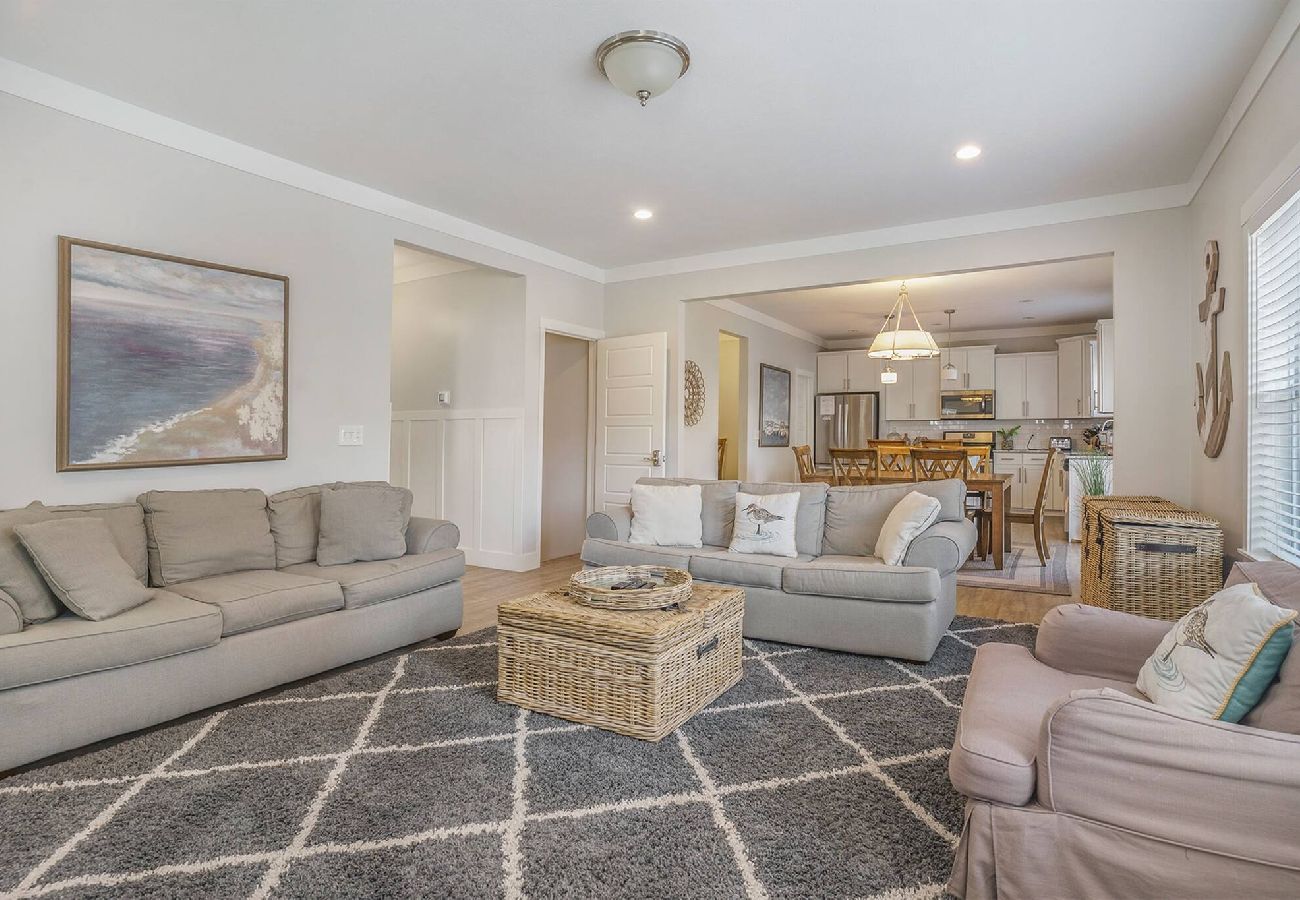 Open living room with sofas, accent chair, wicker coffee table, and view into kitchen and dining area at Bridgewater Cottage