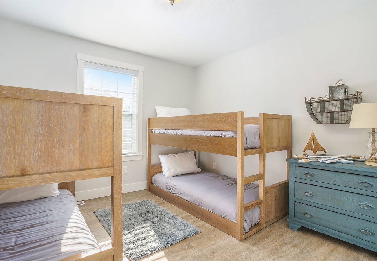 Bedroom with two wooden bunk beds, dresser, and coastal decor at Bridgewater Cottage