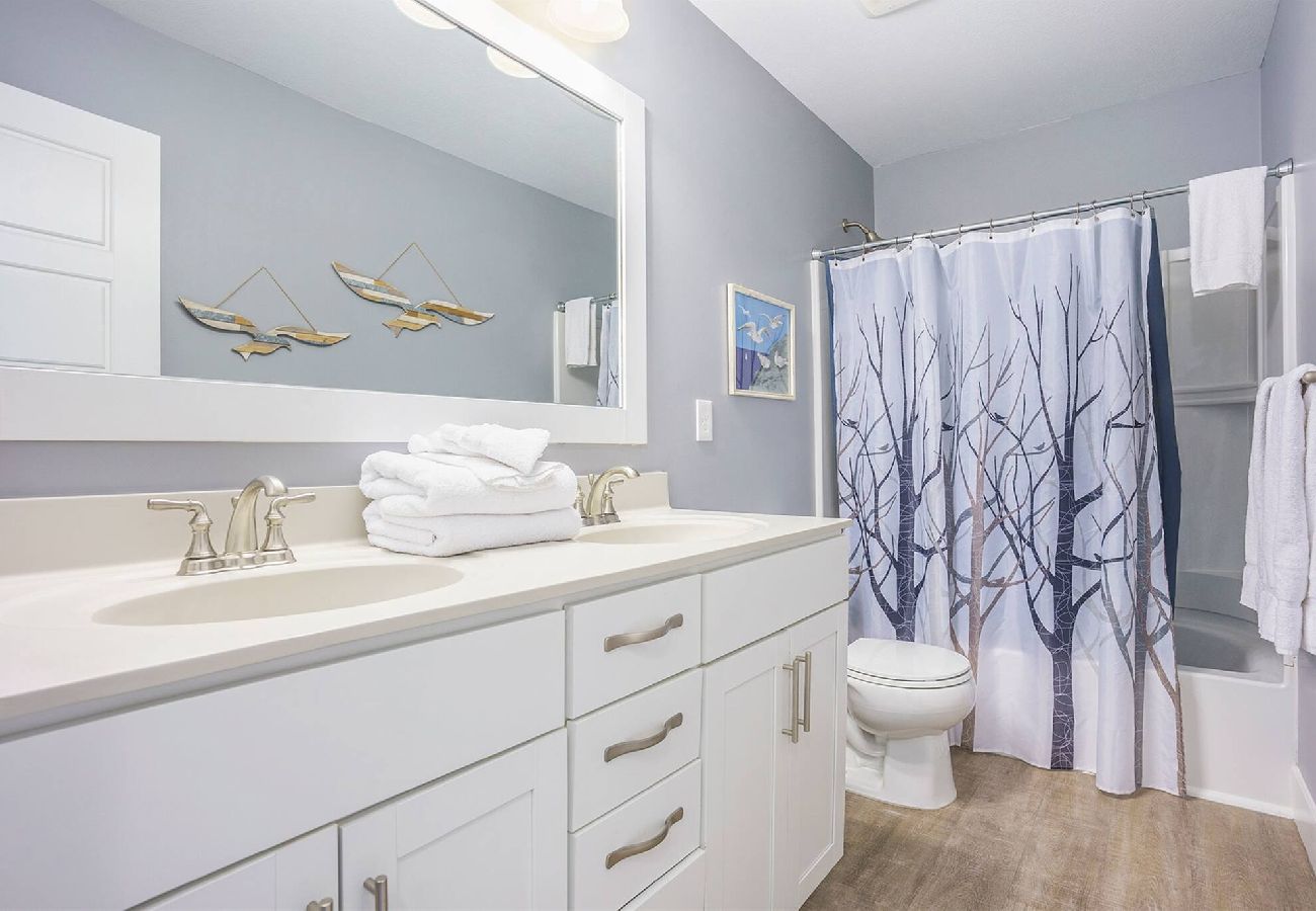 Hall bathroom with double-sink vanity, coastal decor, and shower/tub combo at bridgewater Cottage
