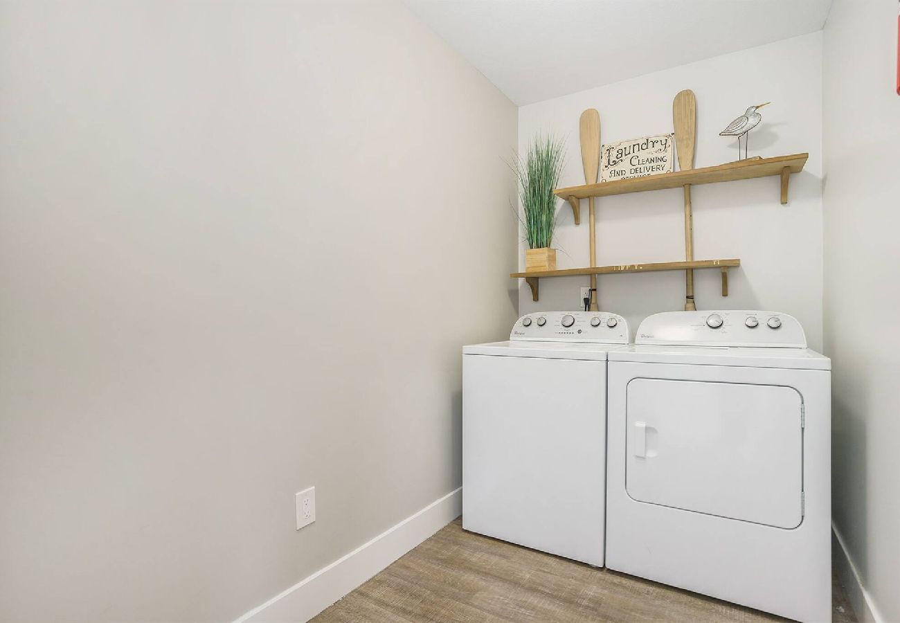 Laundry room with full-size washer, dryer, and coastal wall shelves at Bridgewater Cottage