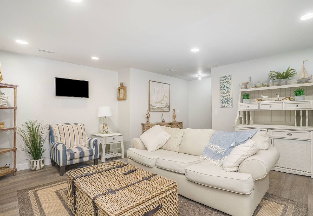 Basement living room with sofa, striped chair, wicker coffee table, and coastal decor at Bridgewater Cottage