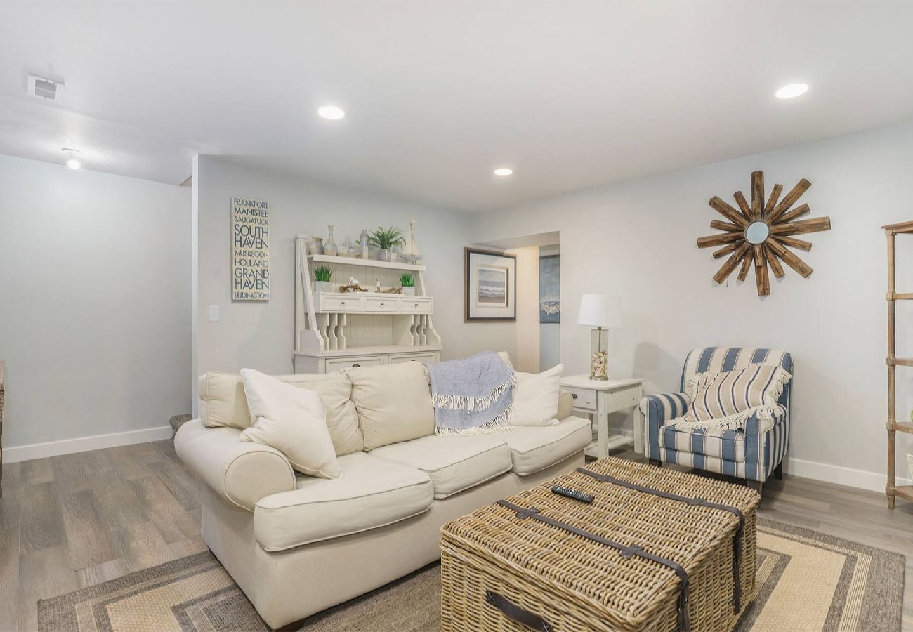 Basement living area with sofa, striped chair, wicker coffee table, and coastal decor at Bridgewater Cottage