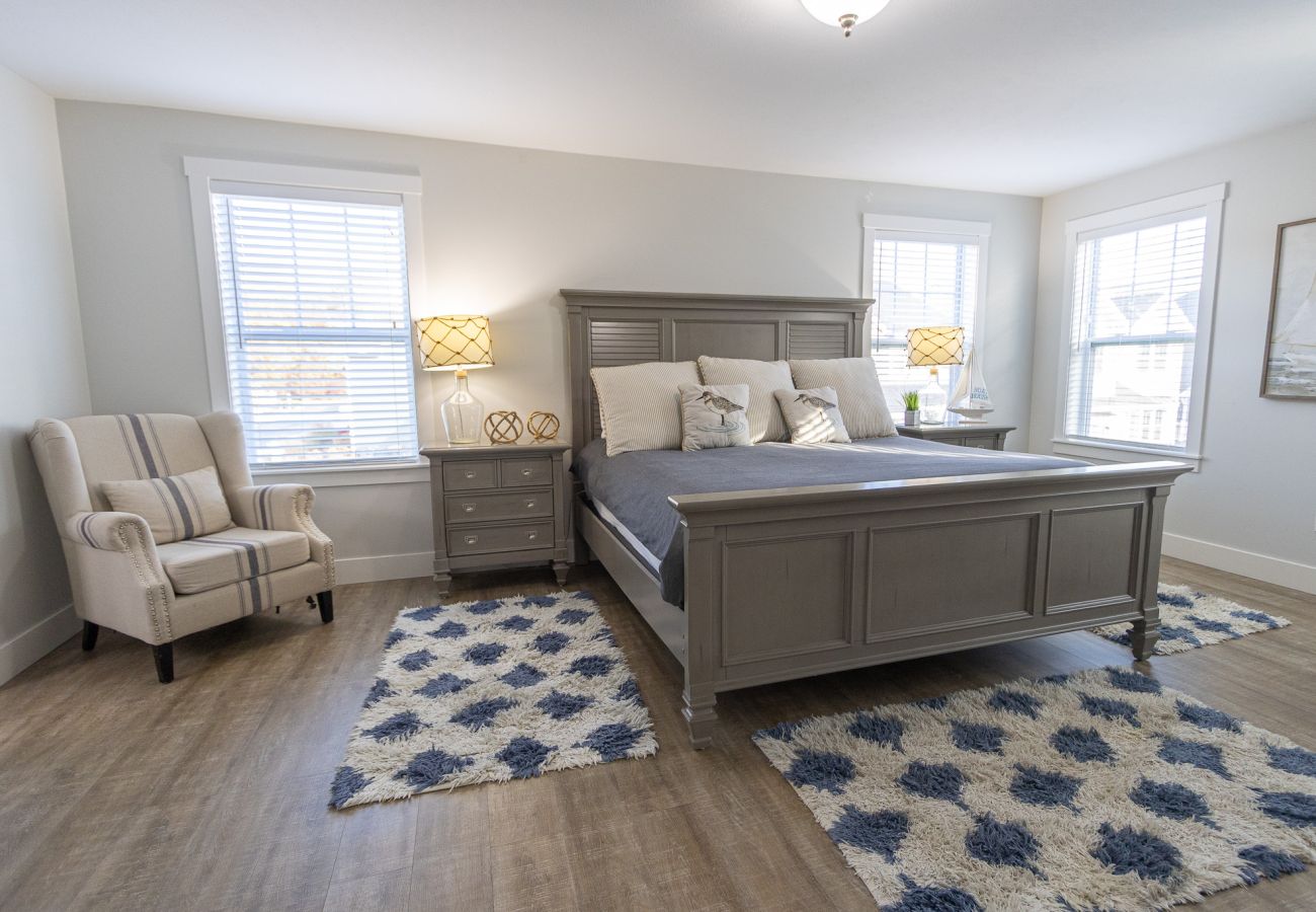 Primary bedroom with king bed, accent chair, and bright windows at Bridgewater Cottage 