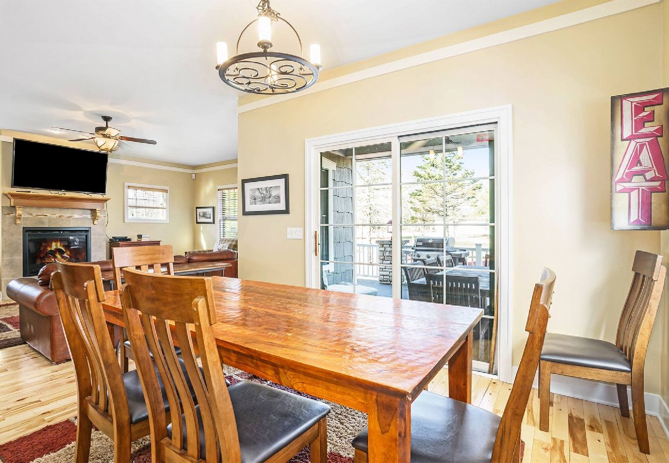 Dining room with wooden table and chairs, sliding doors to the patio, and the view of the living room with fireplace