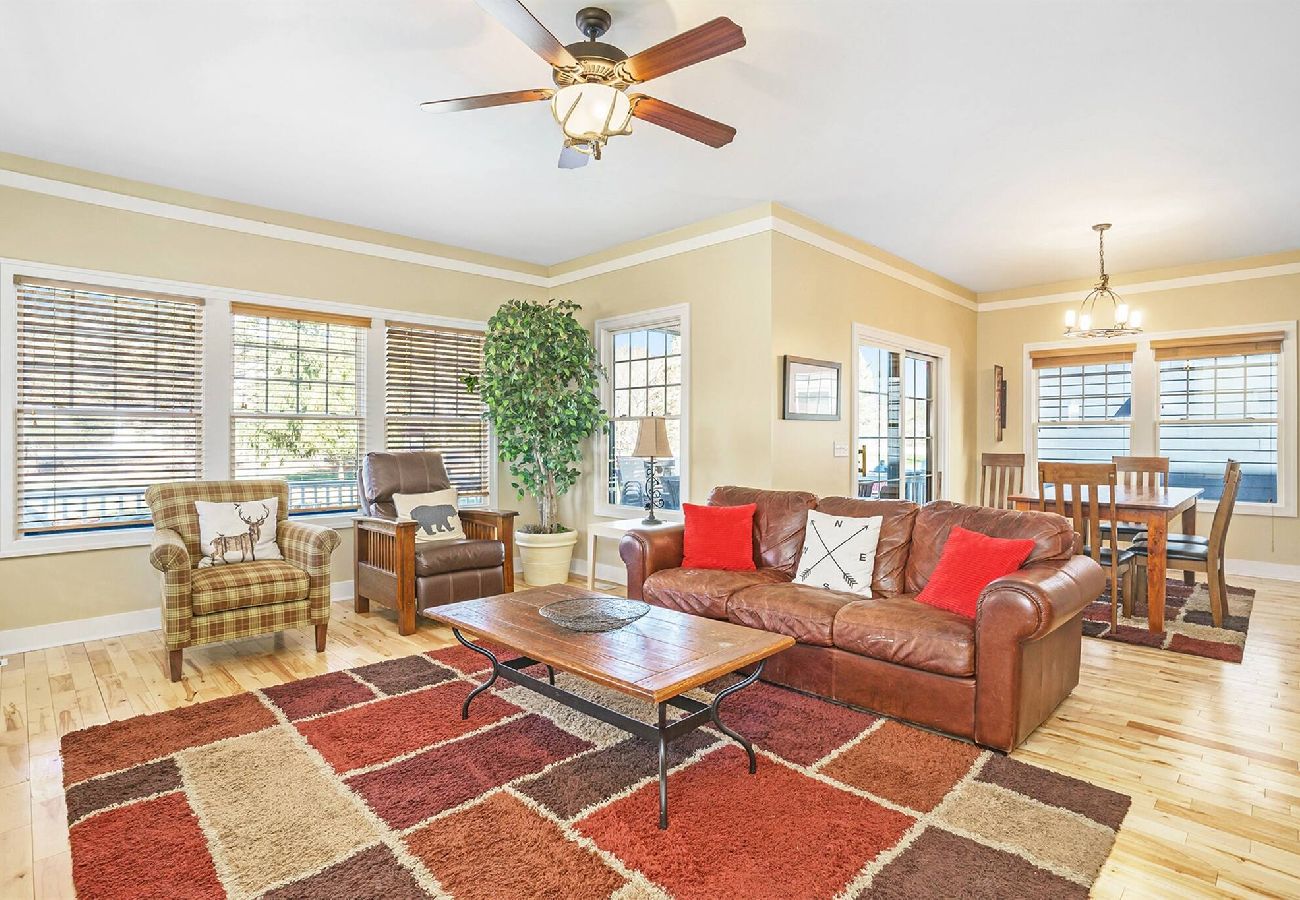 Living room with leather sofa, accent chairs, large windows, and open view to the dining area at Daydreamer Cottage