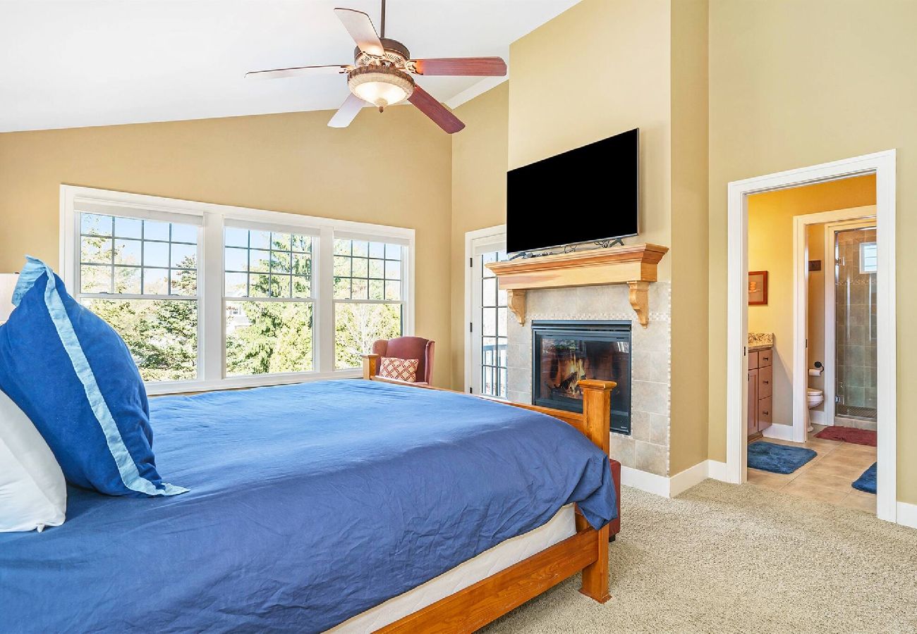 Primary bedroom with king bed, large windows, fireplace and wall-mounted TV