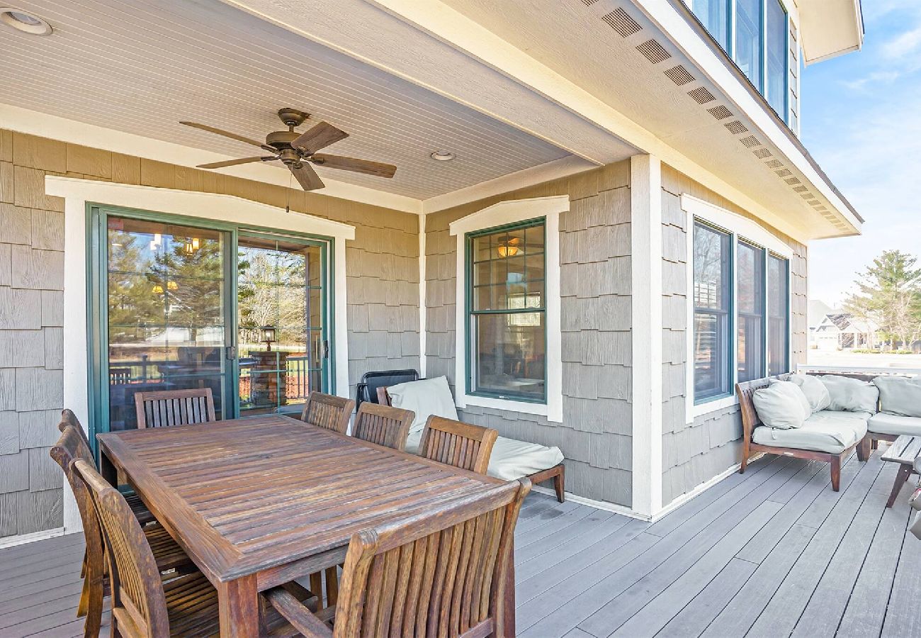 Covered patio with a wooden outdoor dining table, chairs, ceiling fan, and cushioned lounge seating at the Harbor Club