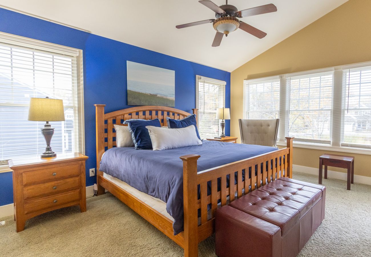 Primary bedroom with king bed, blue accent wall, large windows, and cozy seating 
