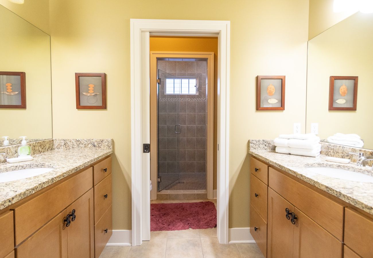 En-suite bathroom with granite vanities, wood cabinets, and walk-in tiled shower with glass door 