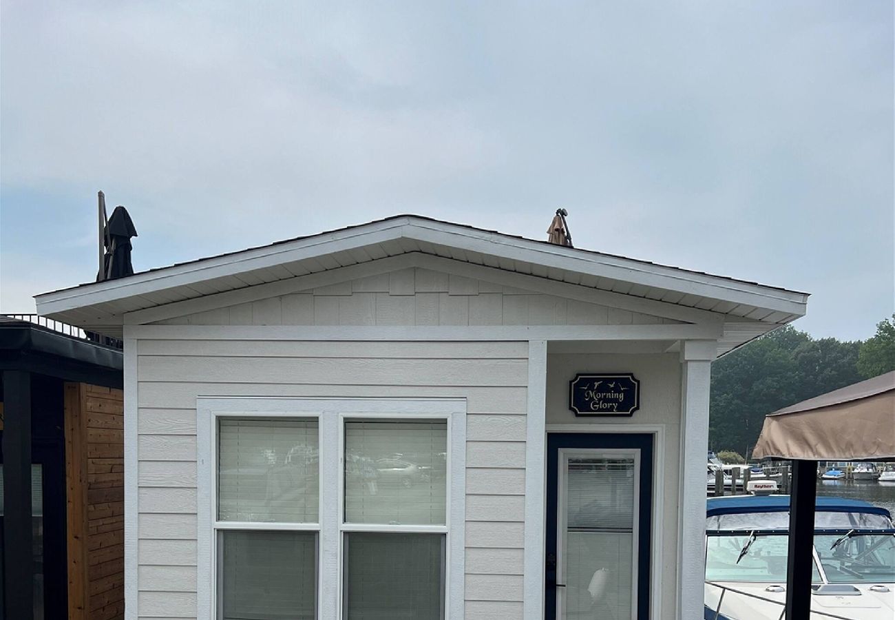Front exterior of the Morning Glory tiny floating cottage with white siding, narrow entry door and marina views