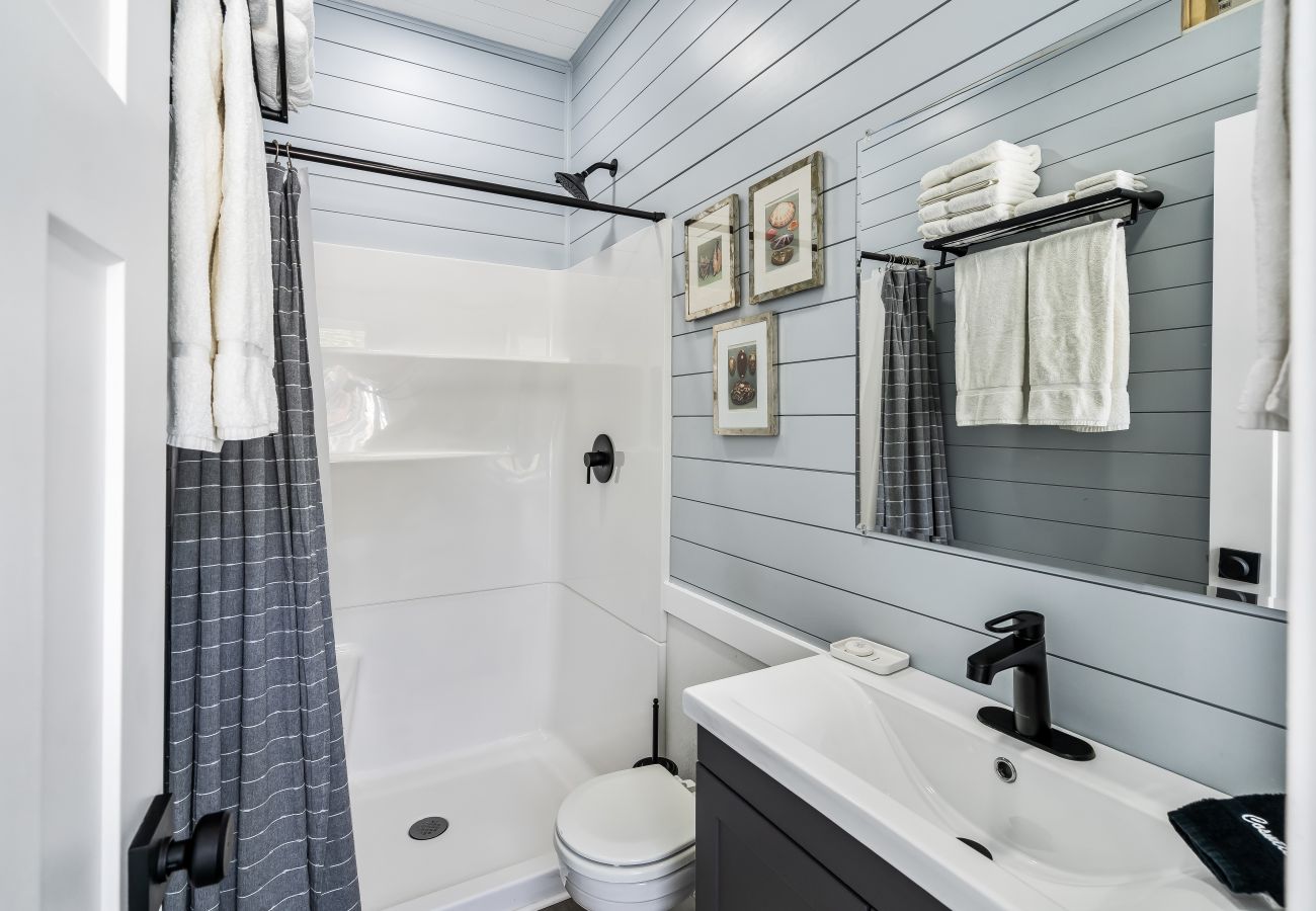 Bright bathroom with full shower, vanity sink, and coastal shiplap walls at Morning Glory floating cottage
