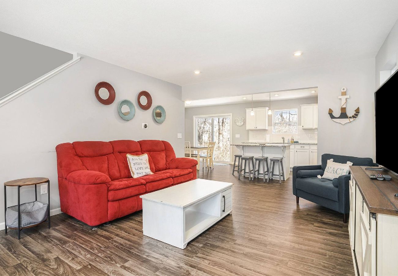 Open living area with red sofa, blue armchair, white coffee table, and view into bright kitchen with bar stools