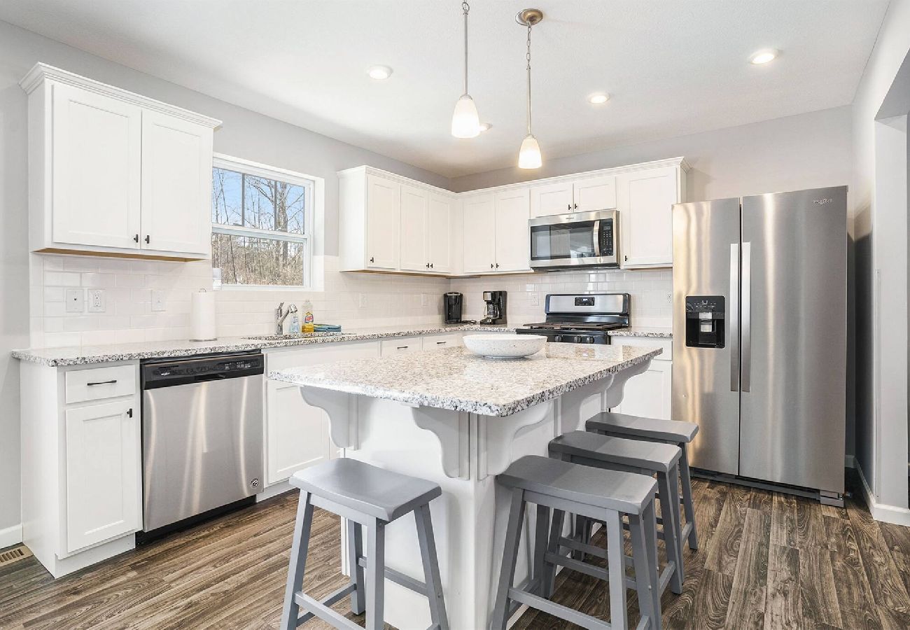 White kitchen with stainless steep applainces, large island, and bar stools