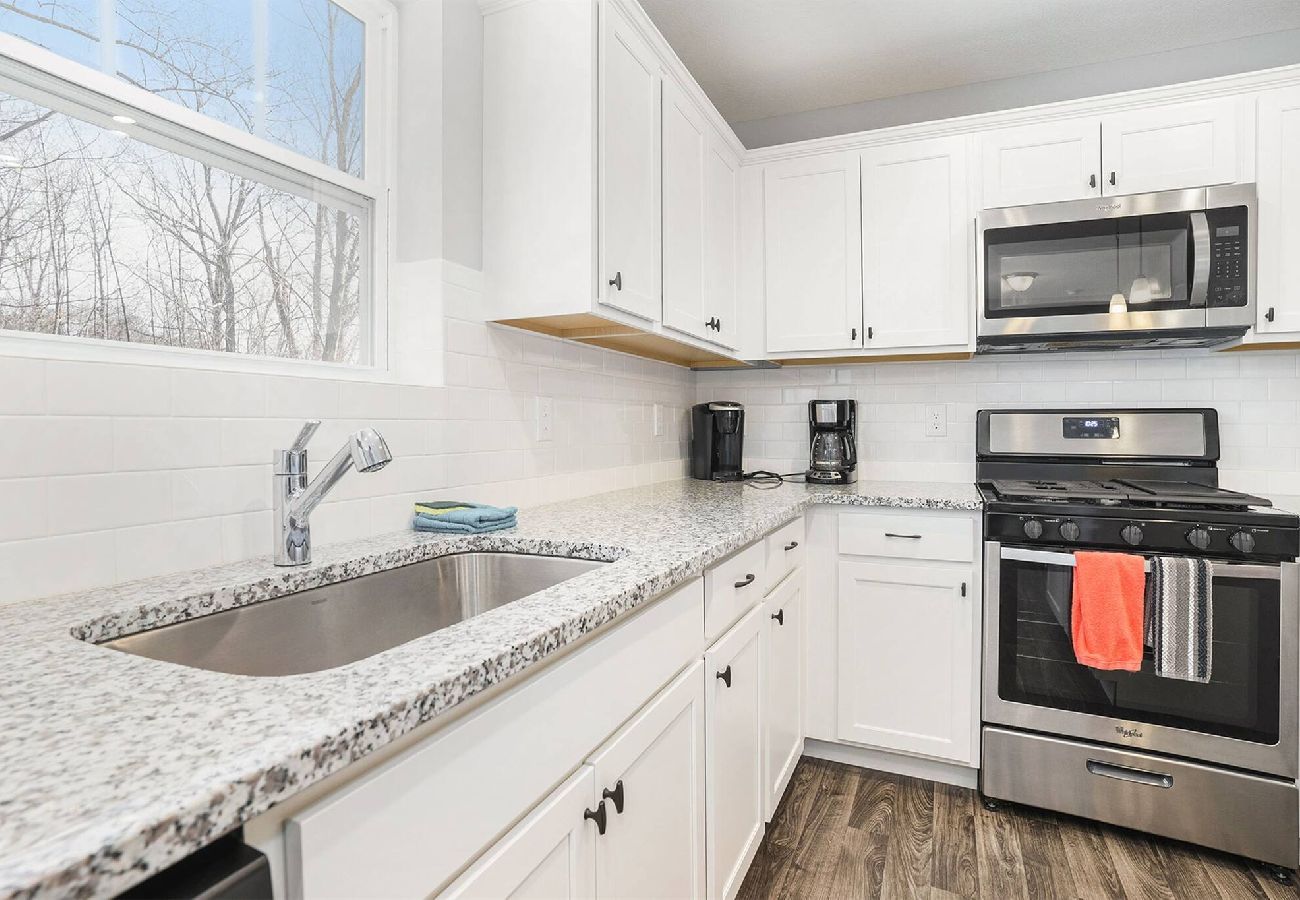 White kitchen with granite countertops, stainless steel stove and microwave, and large sink under window