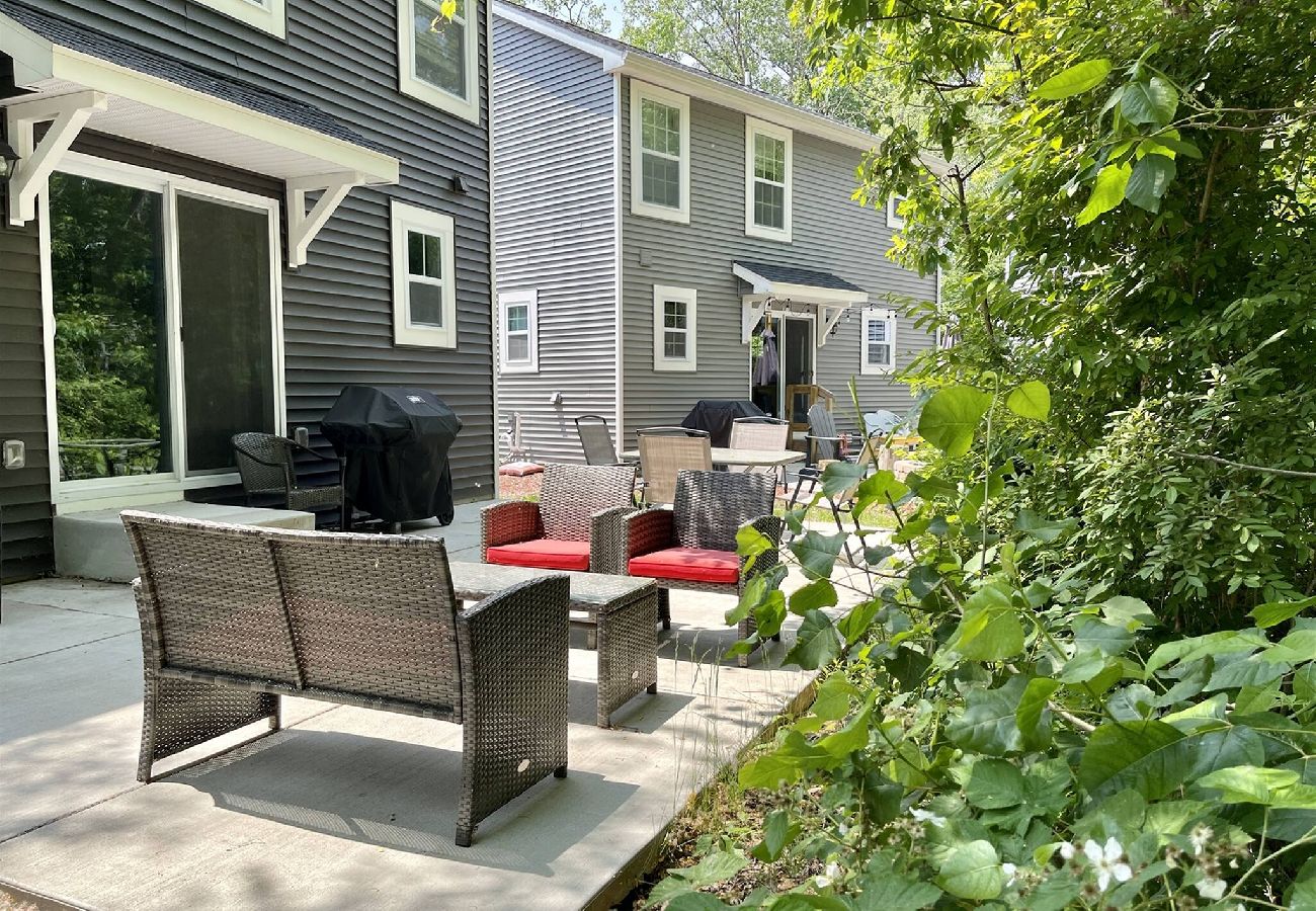Outdoor patio area with wicker seating, grill, and wooded greenery behind home