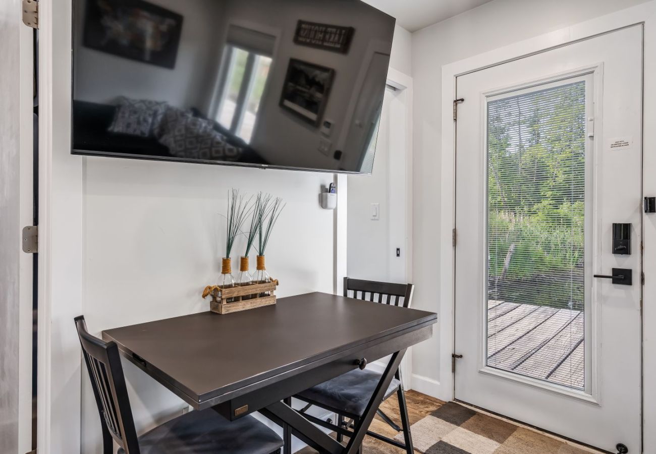 Small dining table with two chairs, wall-mounted TV, and door overlooking the waterfront at Aqua Vista Floating Cottage