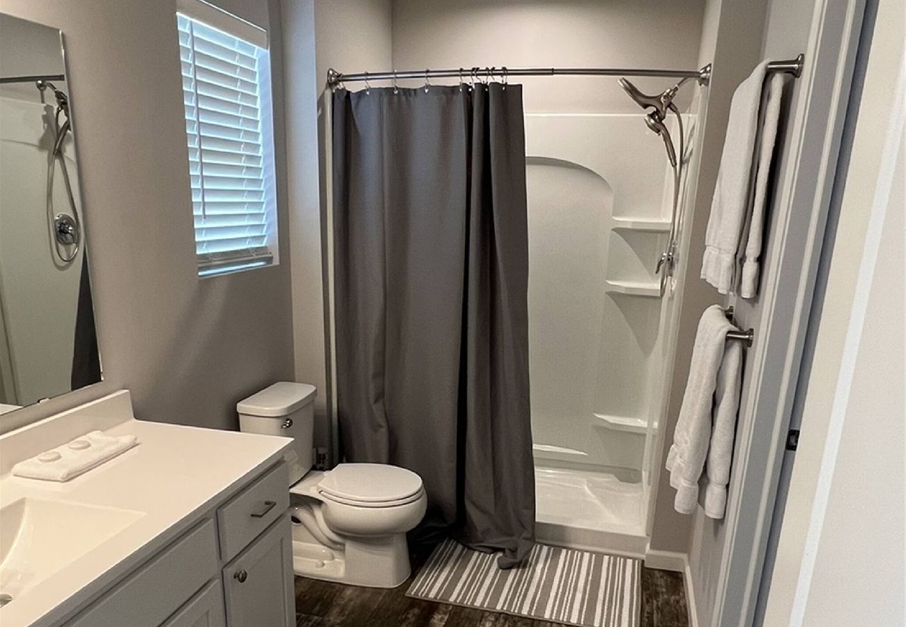 primary bathroom at Harbor Pointe with large vanity, walk-in shower, toilet, and doorway leading to a walk-in closet.