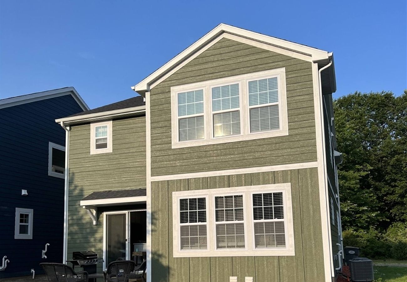 Rear exterior of Harbor Pointe vacation home with green siding, white trim, sliding door, and outdoor seating area