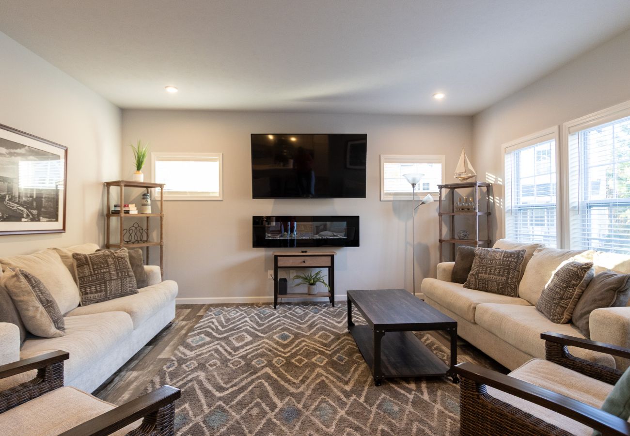 Harbor Pointe living room with two sofas, accent chairs, large wall-mounted TV, and electric fireplace