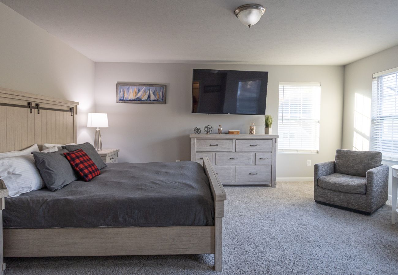 Harbor Pointe primary bedroom with king bed, dresser with mounted TV, and sitting chair