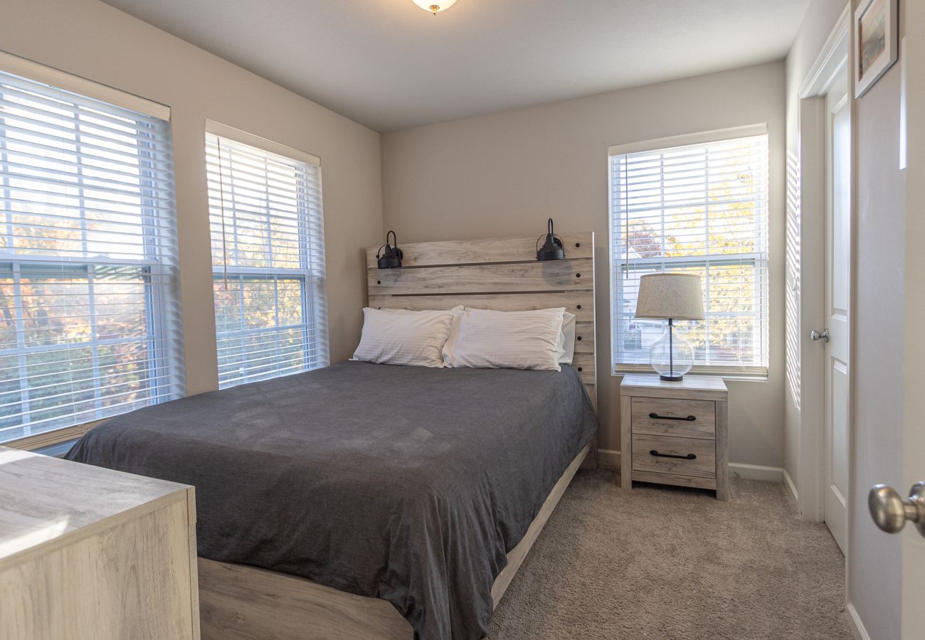 Harbor Pointe bedroom with queen bed, nightstand and lamp, three large windows, and neutral decor