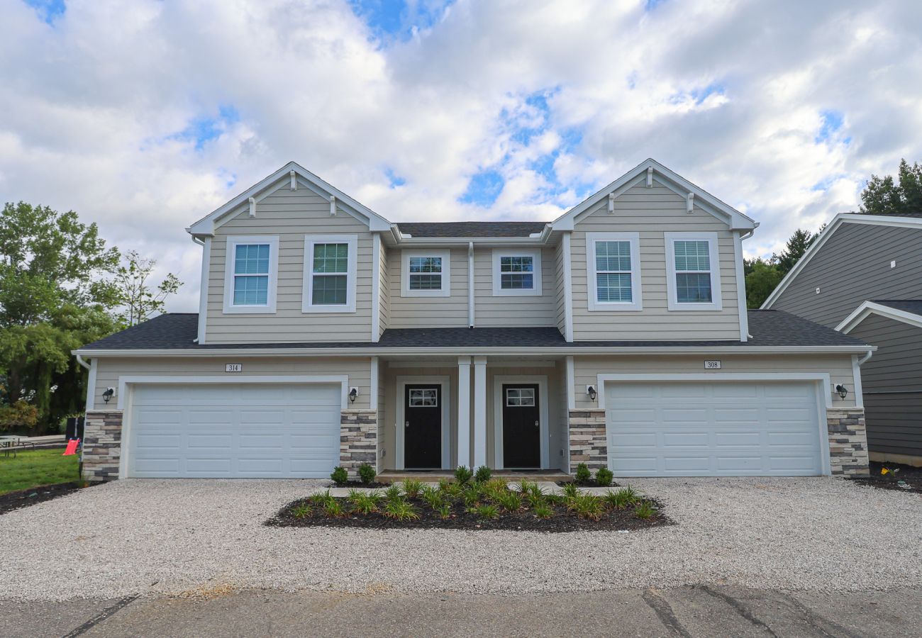 Beige townhome with two-car garage, , stone accents, and shared landscaping