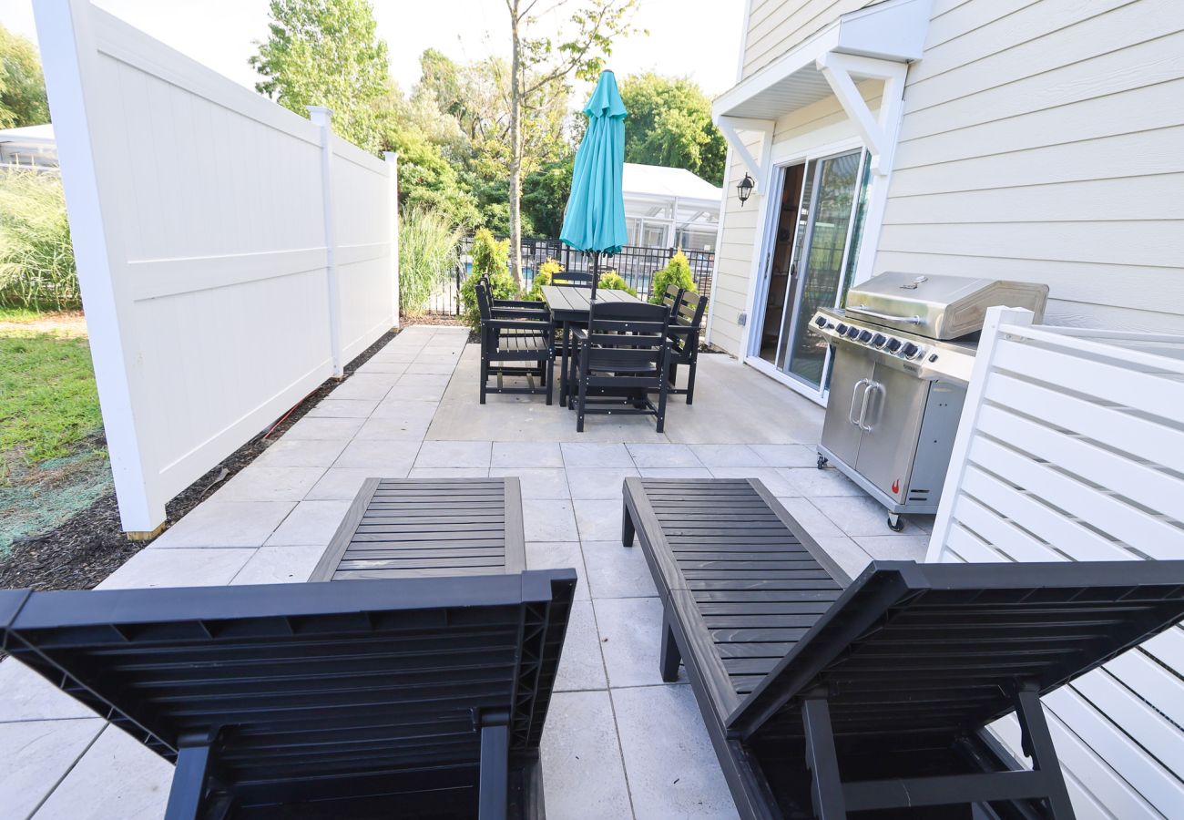 Private patio with two black lounge chairs, outdoor dining table with umbrella, and stainless-steel grill.