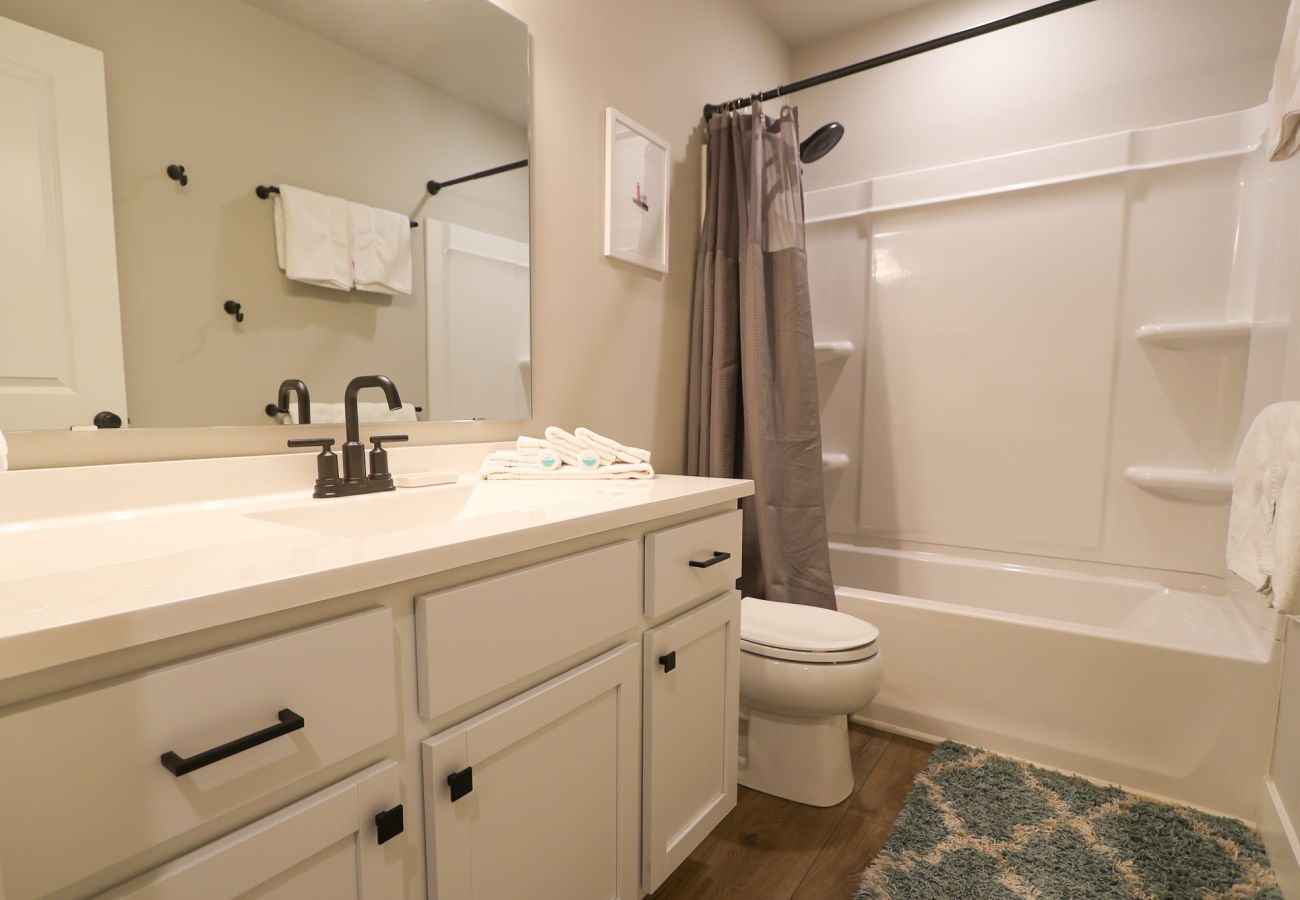 Hall bathroom with white vanity, black fixtures, and shower/tub combo