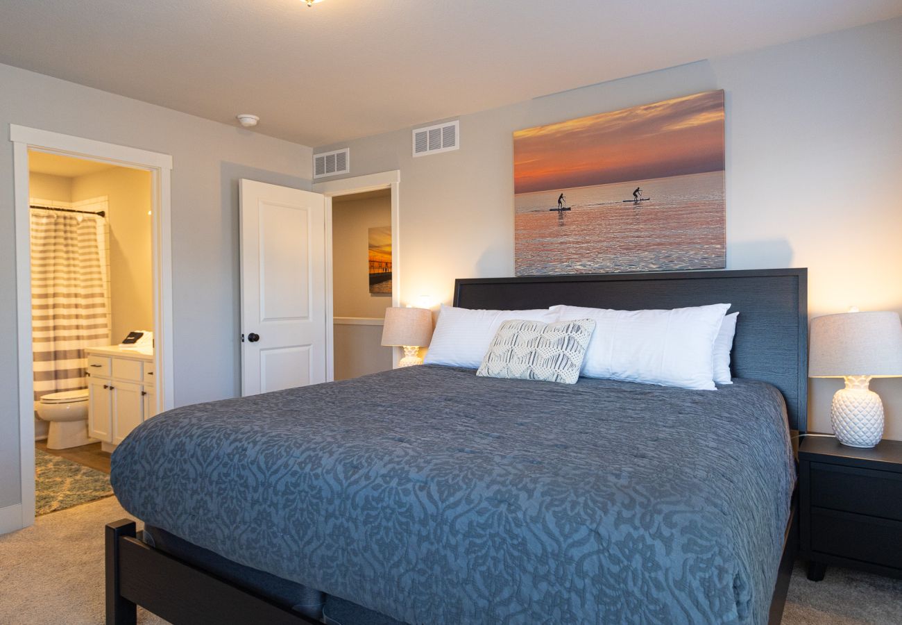 Primary bedroom with king bed, coastal artwork, bedside lamps, dresser with TV, and en-suite bathroom access 