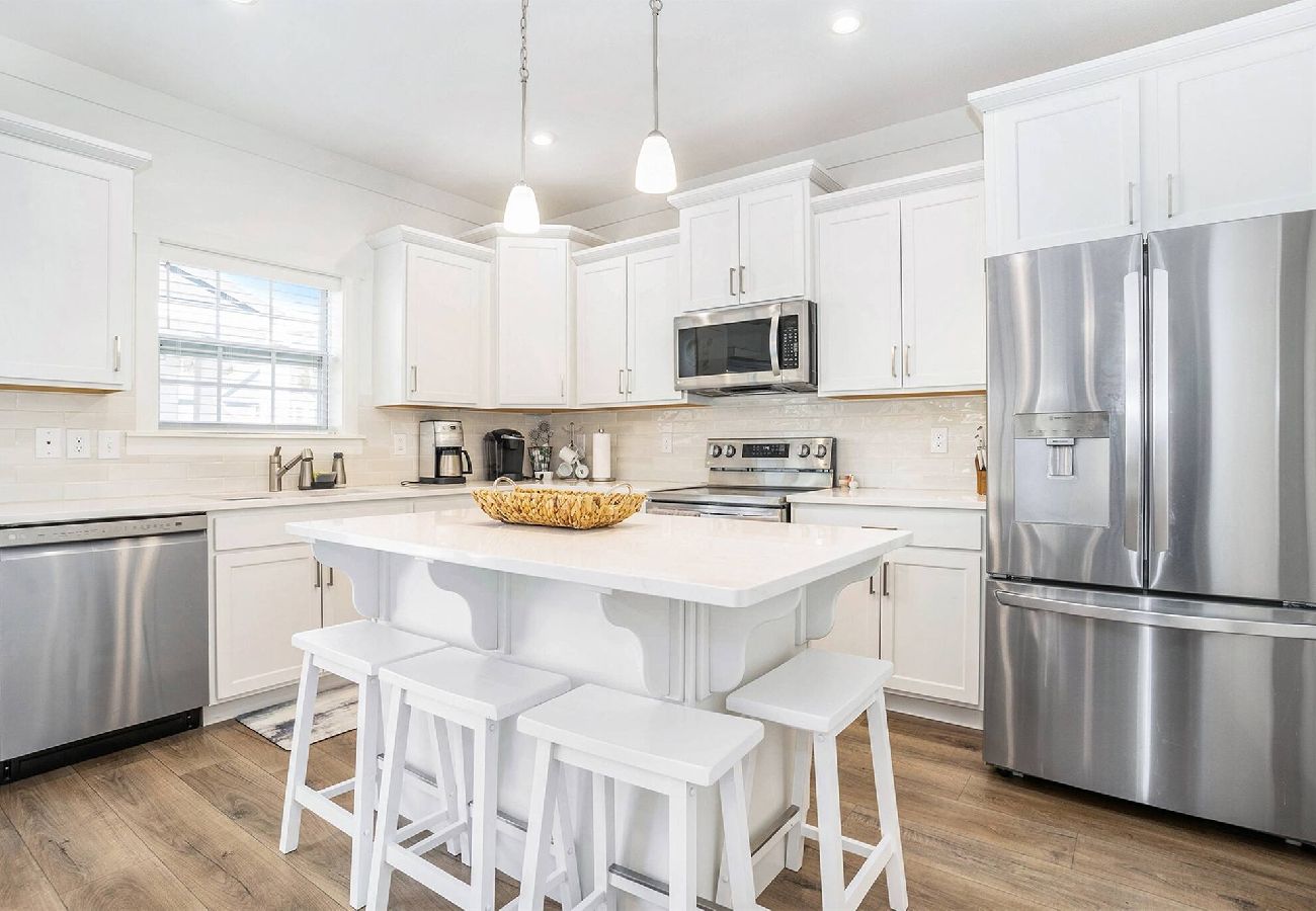 White kitchen with stainless steel appliances, center island with four stools, pendant lighting, and wood-look flooring