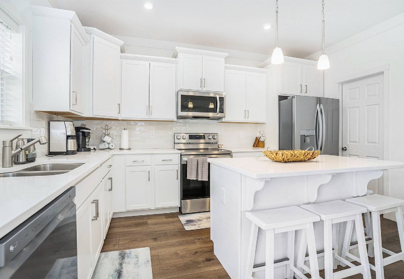 White kitchen with stainless steel appliances, center island, double sink and wood-look flooring