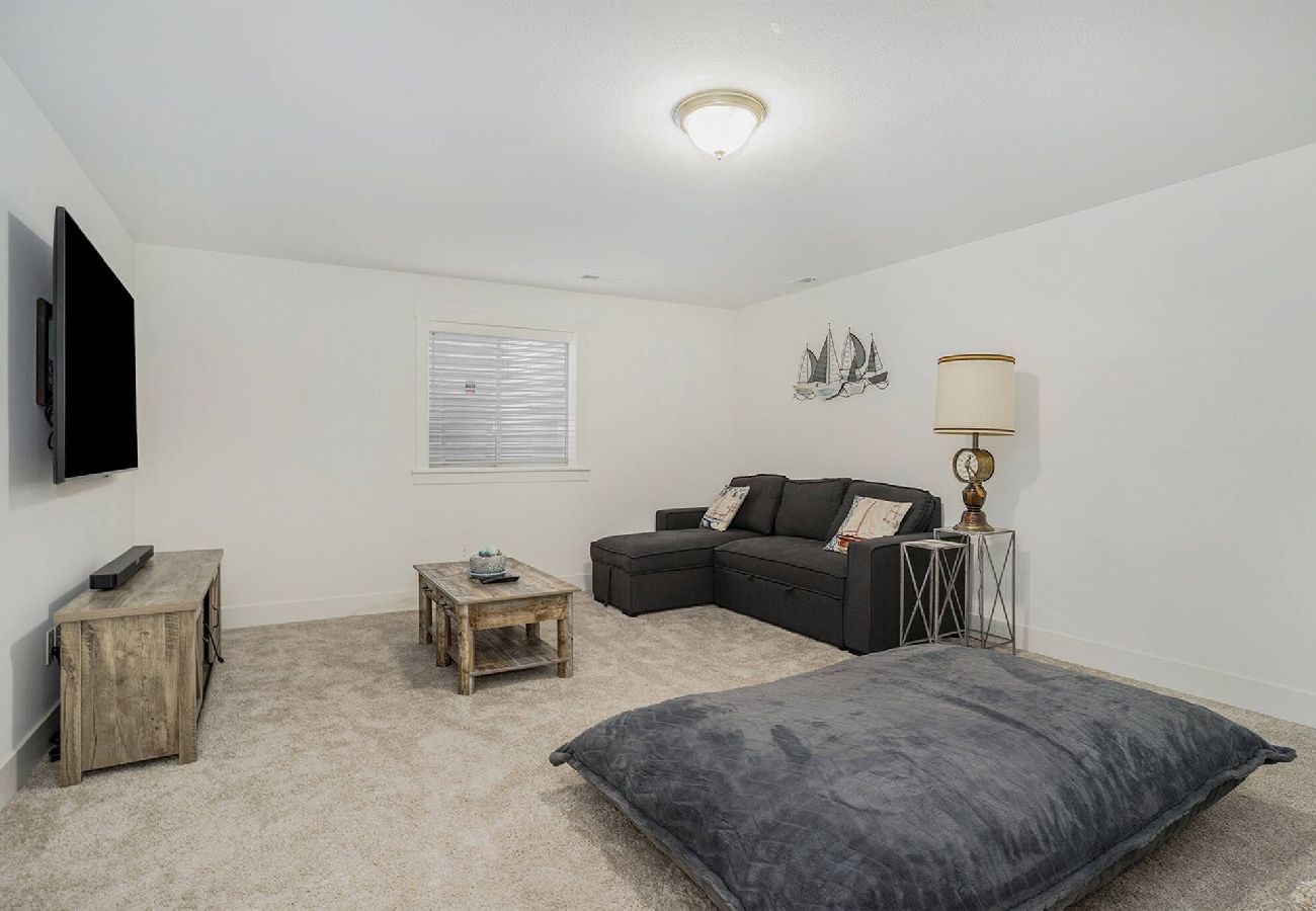 Basement lounge area with sectional sofa, oversized floor pillow, and wall-mounted TV