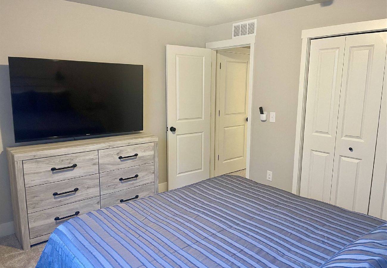 Basement bedroom with large flat-screen TV, wood dresser, and double-door closet