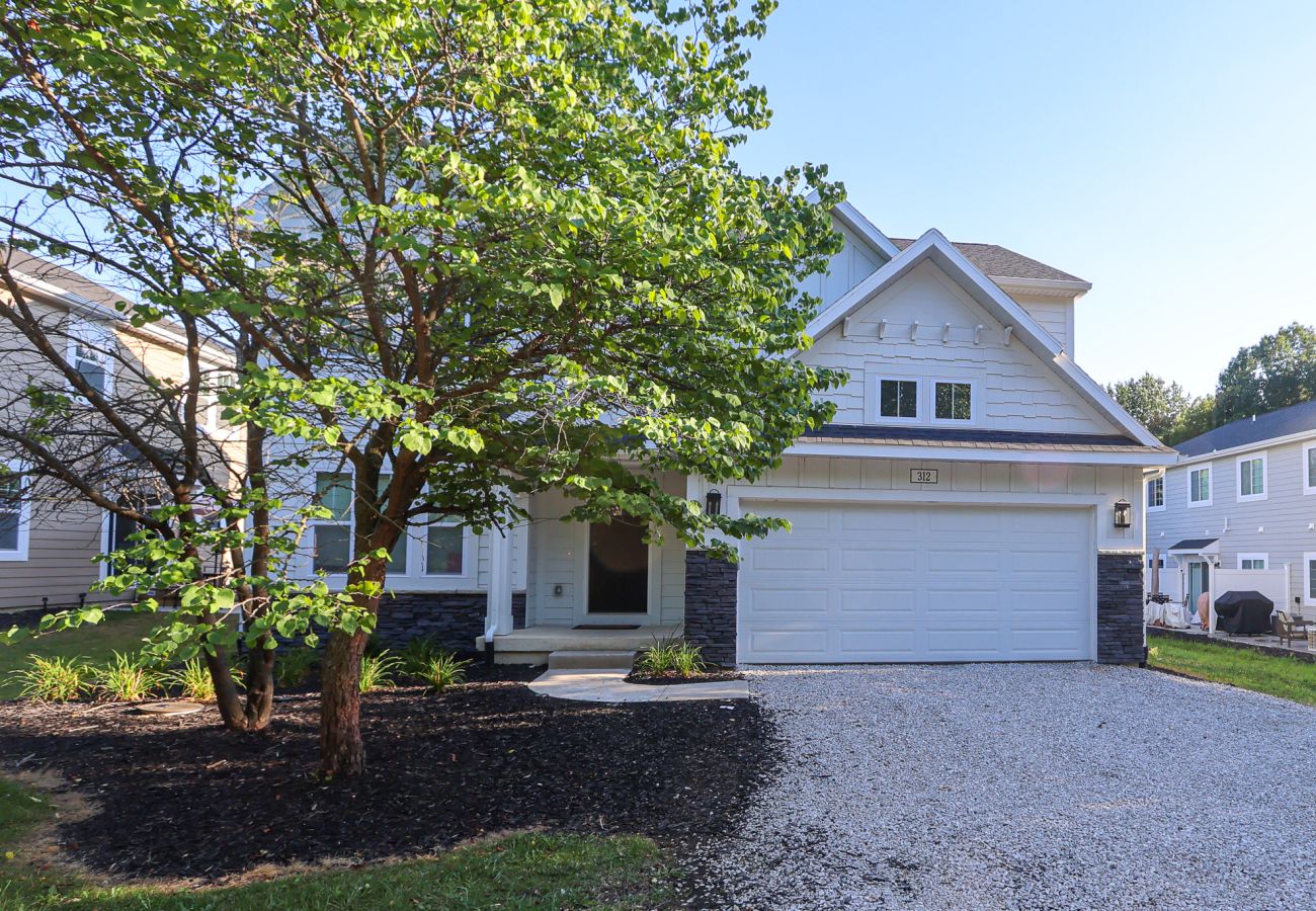 Front exterior of Northside Retreat with large tree, modern white siding, and gravel driveway in South Haven, Michigan
