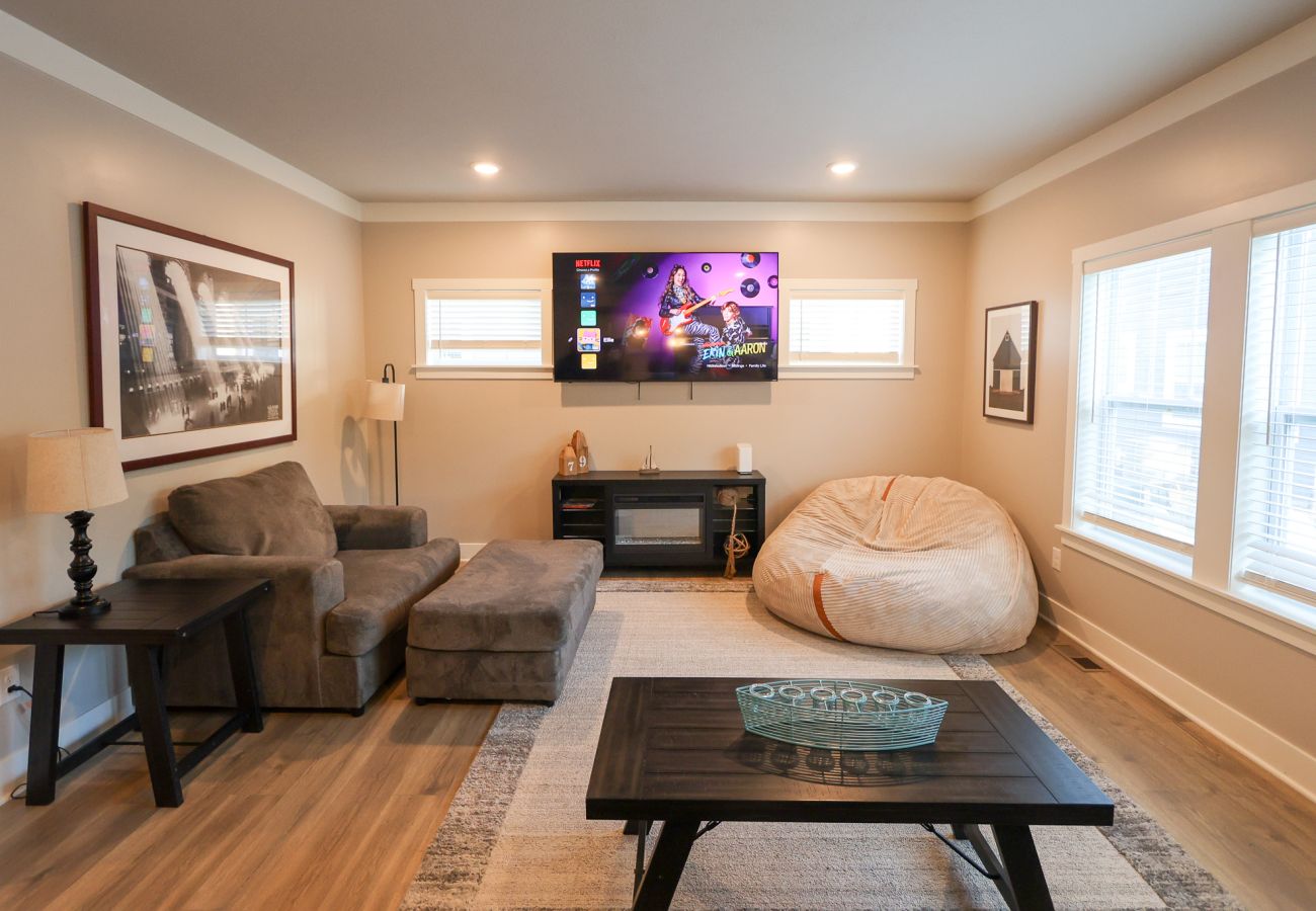 Living room with large mounted TV, sofa and armchair, wood coffee table, and bright windows letting in natural light 
