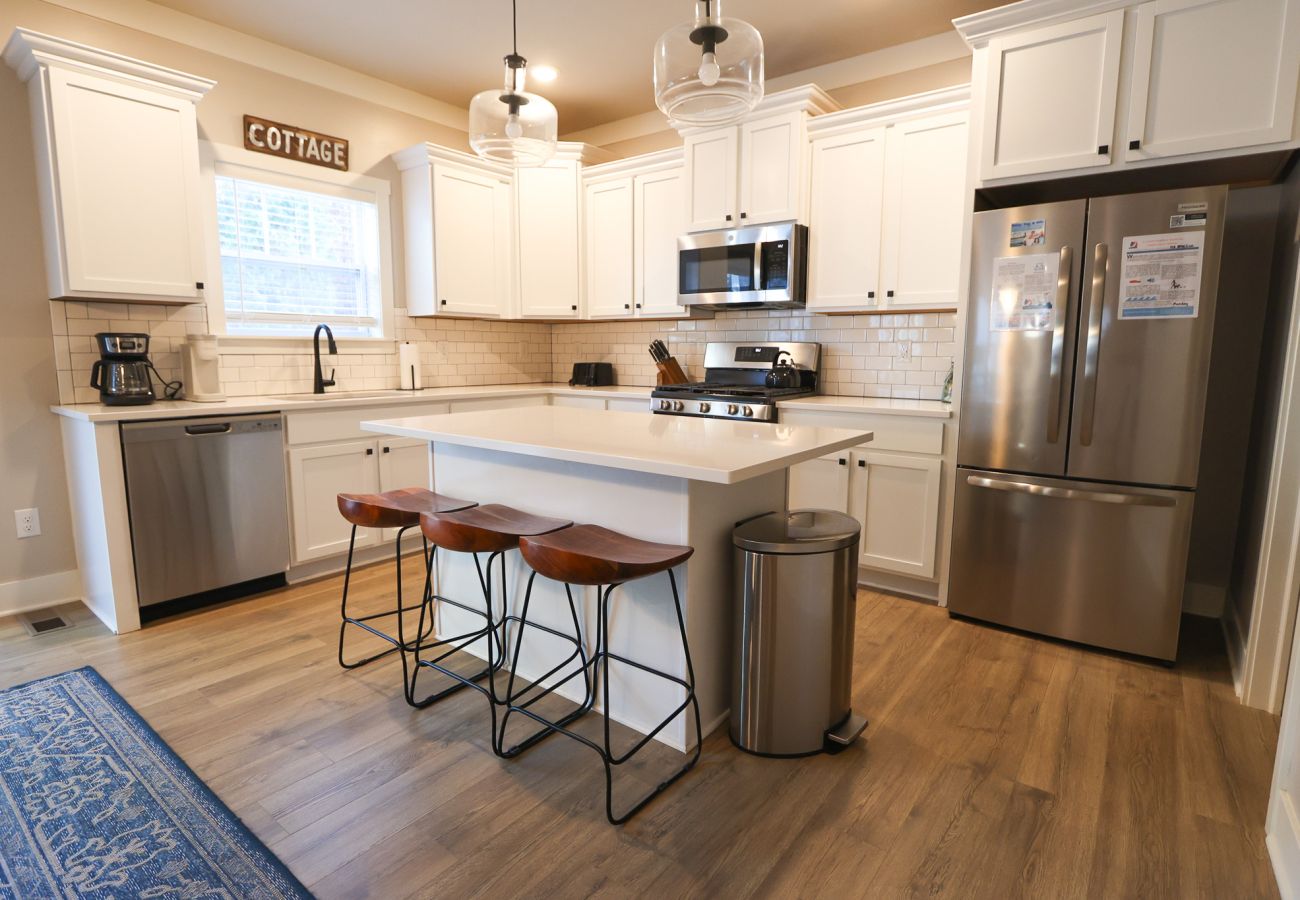 Bright modern kitchen with white cabinets, stainless-steel appliances, center island seating, and wood floors.