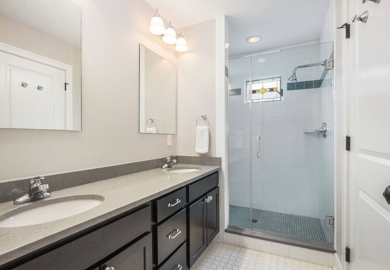 Bright primary bathroom with double sinks and a large walk-in glass shower in South Haven