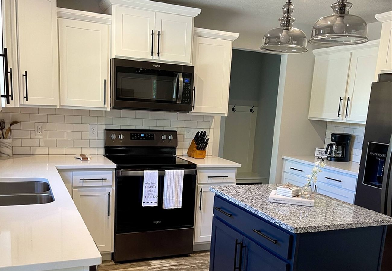 Bright kitchen with white cabinets, granite island, stainless appliances, and pendant lighting 