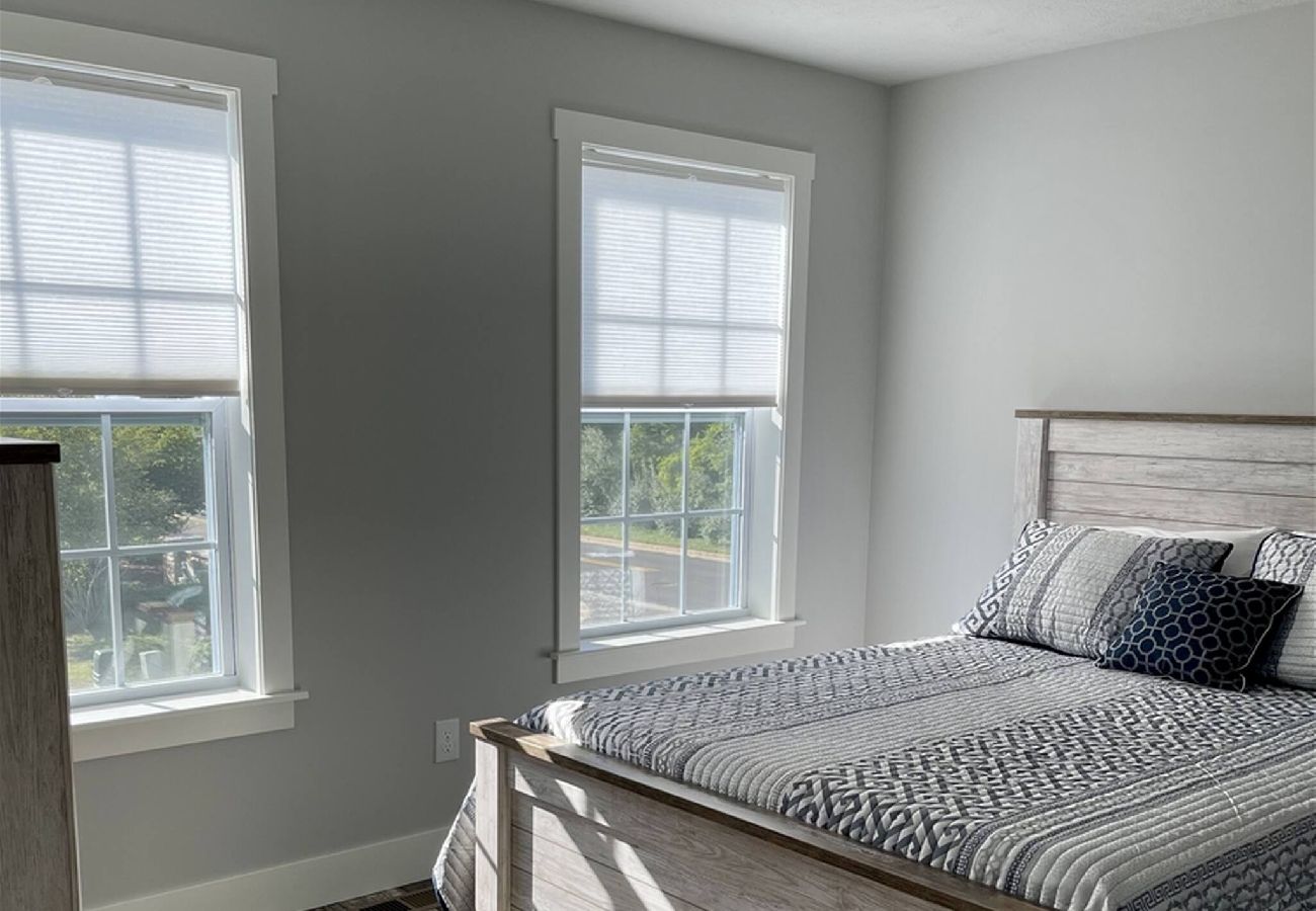 Light-Filled bedroom with a queen bed, light wood furniture, and two large windows