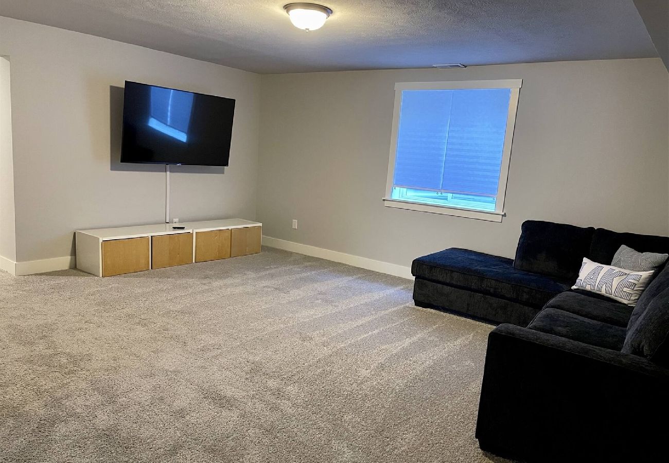 Basement living area with large sectional sofa, mounted flat-screen TV, and carpeted flooring