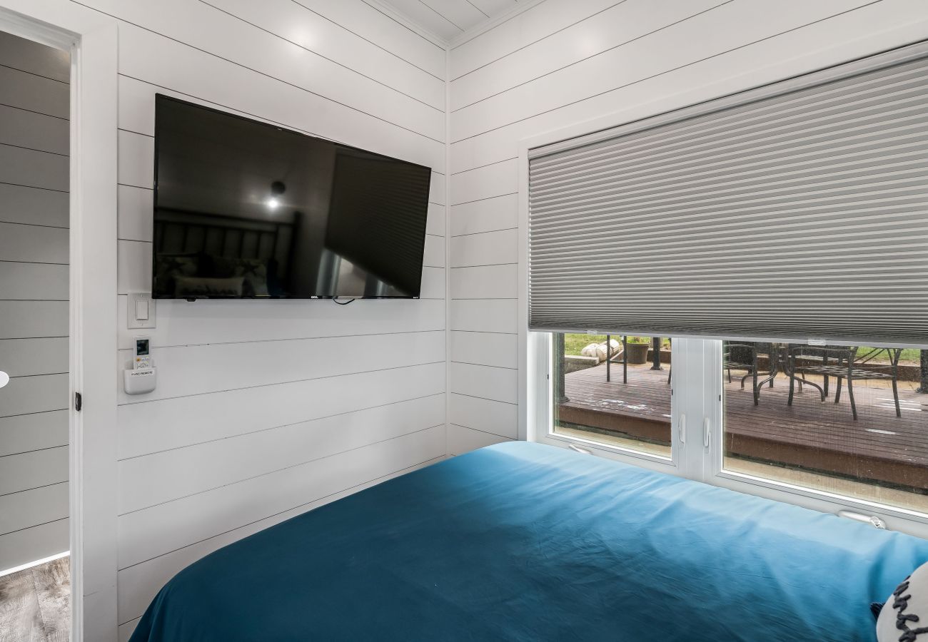 Small bedroom at Shoreside Haven with a mounted flat-screen TV and window overlooking the outdoor deck