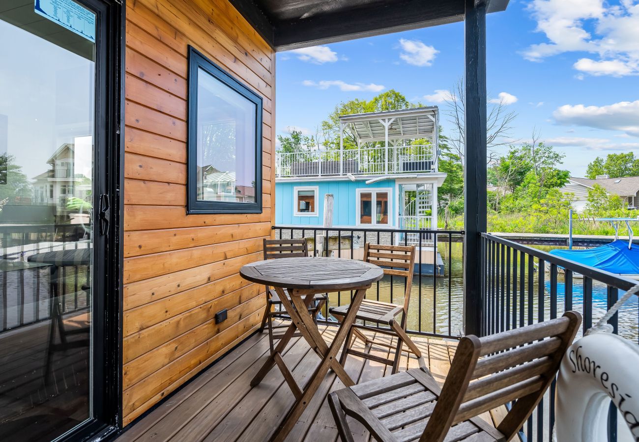 waterfront deck at Shoreside Haven with bistro table, chairs, wood siding, and views of neighboring floating cottages. 
