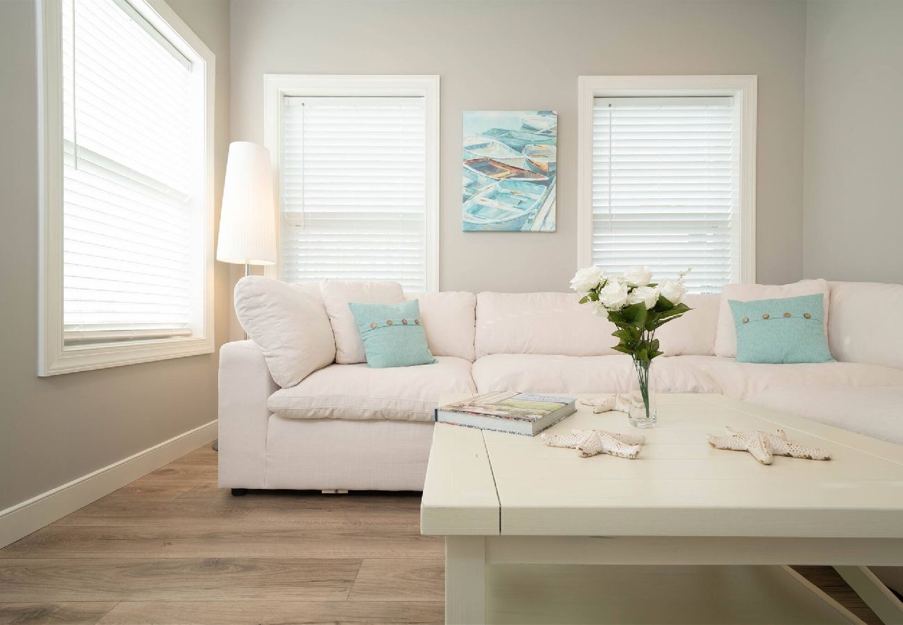 Light-filled sitting area with a soft sectional sofa, coastal pillows, wall art, and a white coffee table with decor