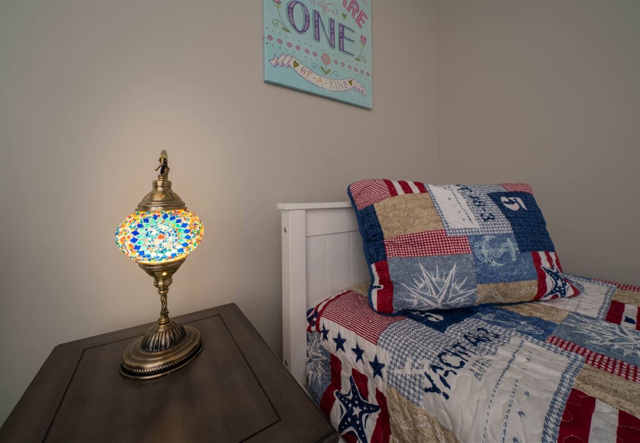 Bedroom with a patriotic patchwork quilt on a twin bed and a colorful mosaic bedside lamp on a wooden nightstand
