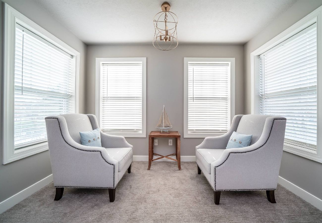 Light-filled sitting area in the primary bedroom with two upholstered armchairs, and large windows