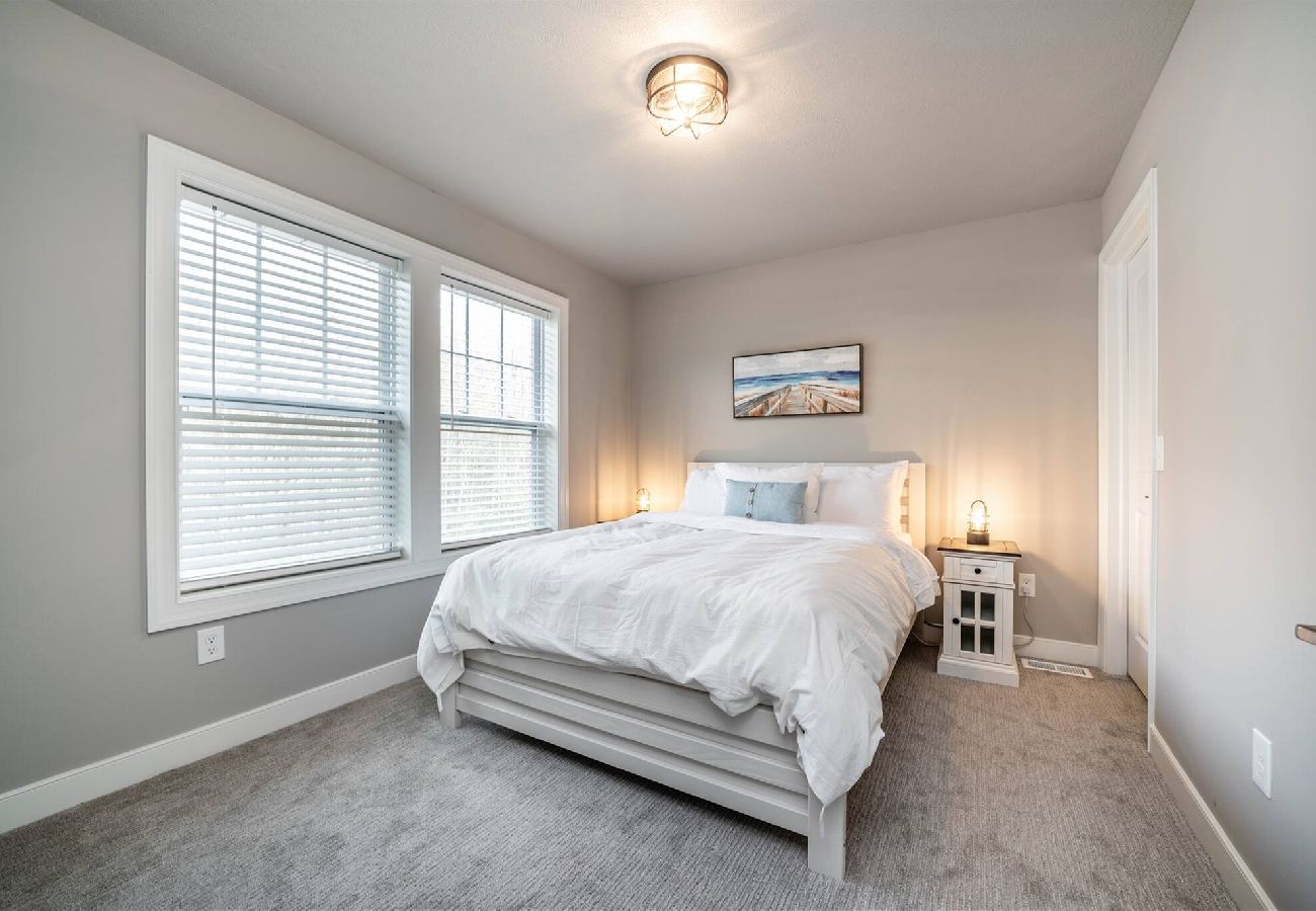 Bedroom with a white bed, bedside table, large windows letting in natural light in a modern neutral-toned space