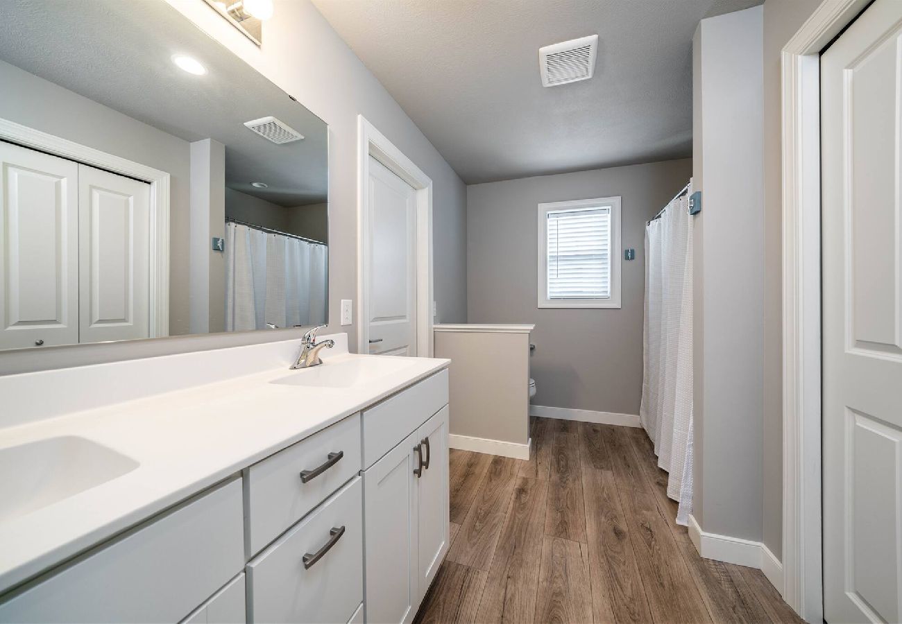Bright bathroom featuring a long double-sink vanity, wood-look flooring, and walk-in shower